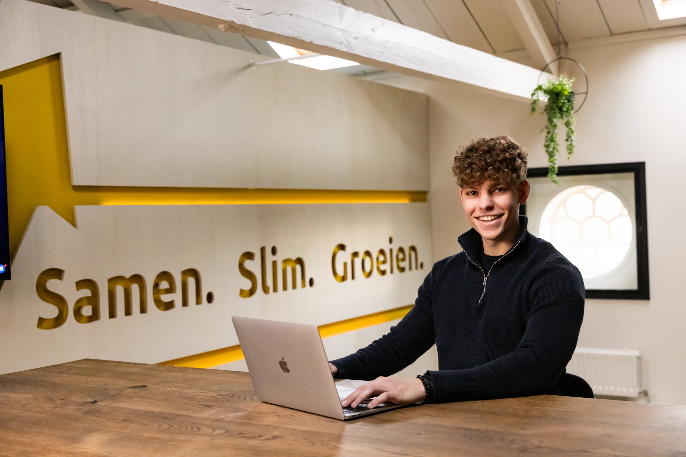 Teamlid van Succesfactor werkt aan de laptop voor de wand Samen. Slim. Groeien.